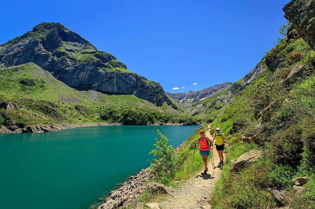 Mann und Frau wandern am See Lac des Gloriettes vorbei zum Cirque d'Estaube, Gavarnie, Nationalpark Pyrenäen, UNESCO Welterbe Monte Perdido, Pyrenäen, Frankreich