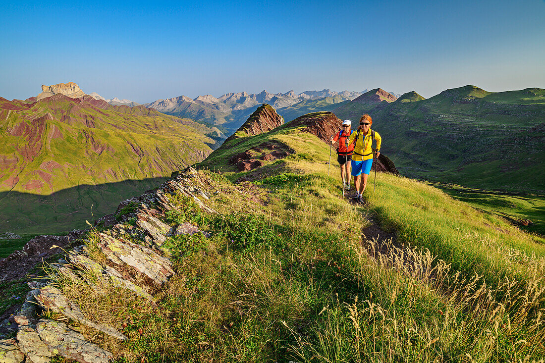 Man and woman hiking across ridges of grass, Castillo d'39; Acher in background, Valle de Hecho, Huesca, Pyrenees, Aragon, Spain