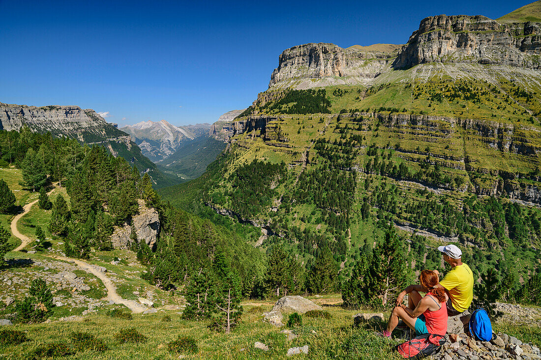 Man and woman hiking take a break and look into the Spanish Grand Canyon in the Ordesa Valley, Rio Arazas Valley, Ordesa Valley, Ordesa y Monte Perdido National Park, Ordesa, Huesca, Aragon, Monte Perdido UNESCO World Heritage Site, Pyrenees, Spain