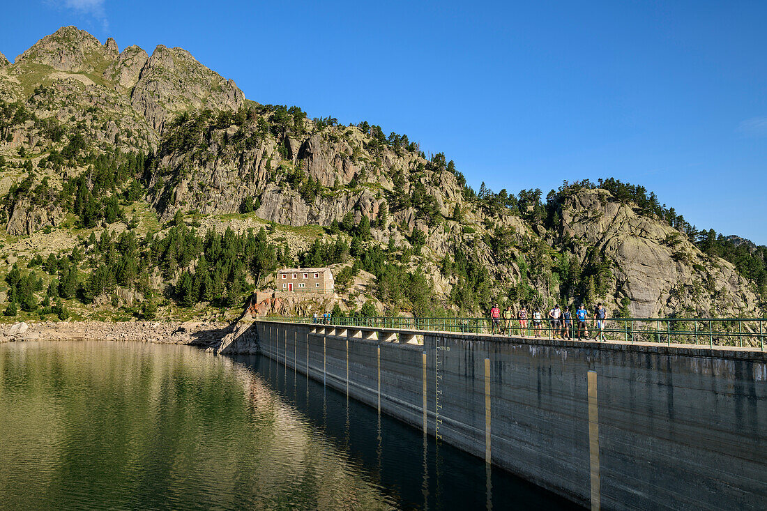 Mehrere Personen beim Wandern gehen über Staumauer am See Lac Major de Colomers, Nationalpark Aigüestortes i Estany de Sant Maurici, Katalonien, Pyrenäen, Spanien