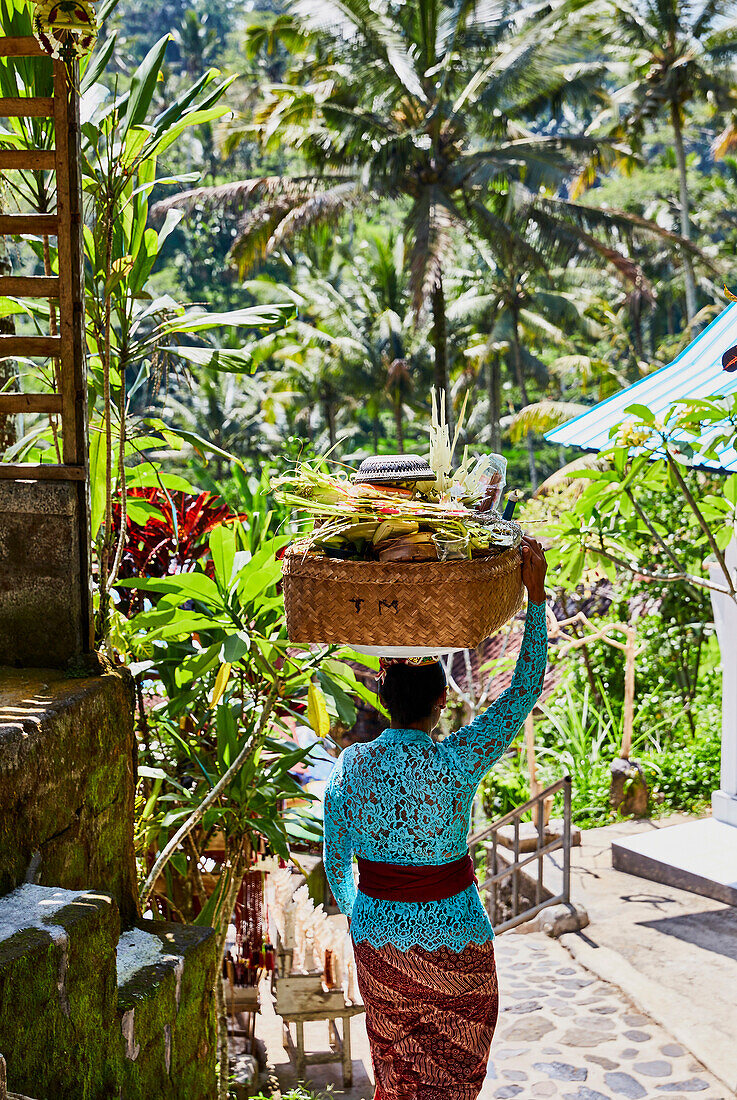 A Balinese woman in traditional dress carries offerings to a prayer service at Gunung Kawi, Gianyar, Bali Indonesia