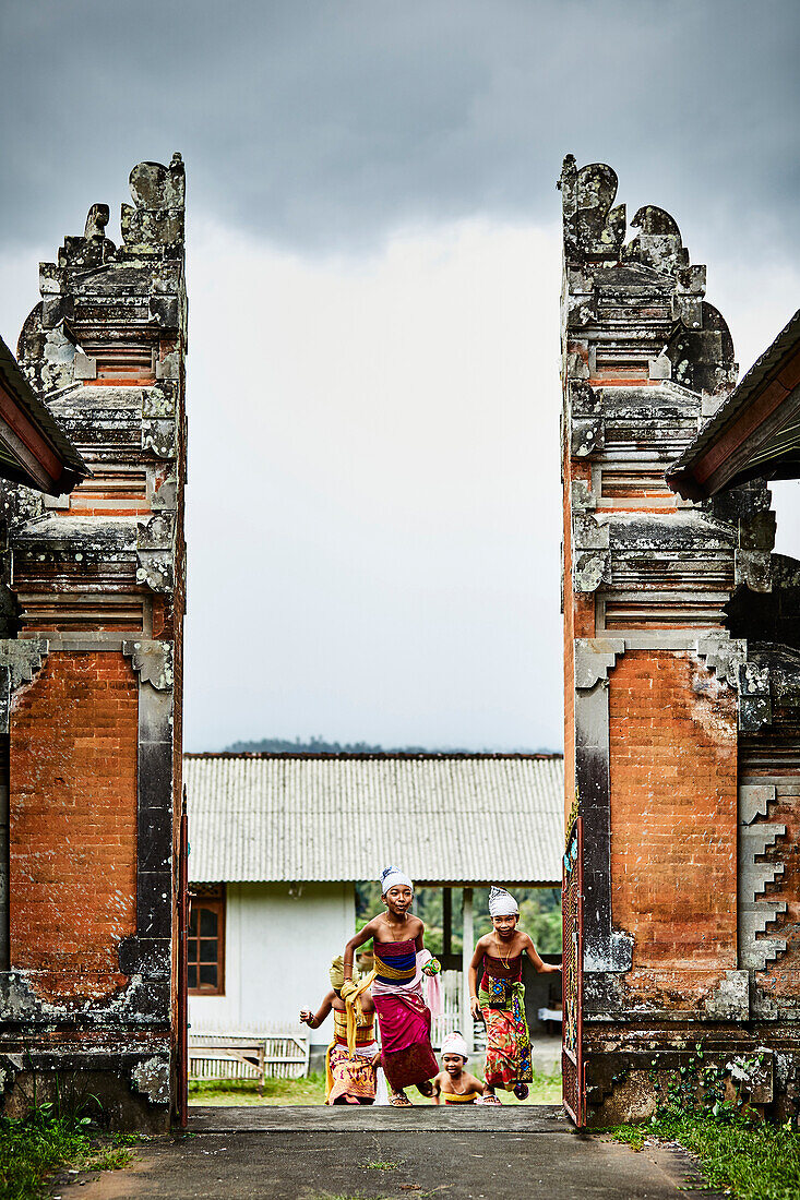 Kinder, die durch die Tore eines Tempels in der Karangasem Region Bali Indonesien laufen, um auf dem Festival von Kuningan zu tanzen.