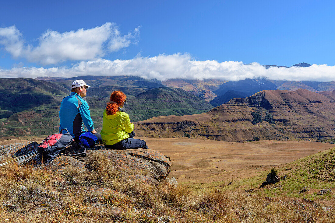 Mann und Frau beim Wandern sitzen auf Felsen und blicken über Drakensberge, Shebas Breasts, Lotheni, Kwa Zulu Natal,  Maloti-Drakensberg, Südafrika