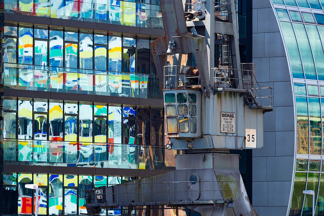 Old crane in front of the glass facade of an office building, the high-rise Colorium is reflected in it, facade with colored glass panels, architect William Alsop, Julo-Levin-Ufers in the Medienhafen, Dusseldorf, North Rhine-Westphalia, Germany, Europe