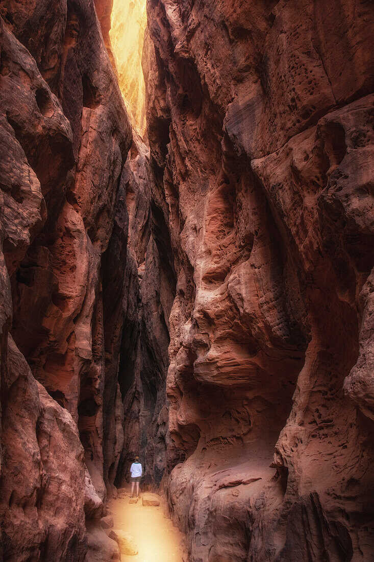 Kleine Person mit weißem Oberteil steht in tiefem engem Canyon, Sonneneinfall, Utah, USA