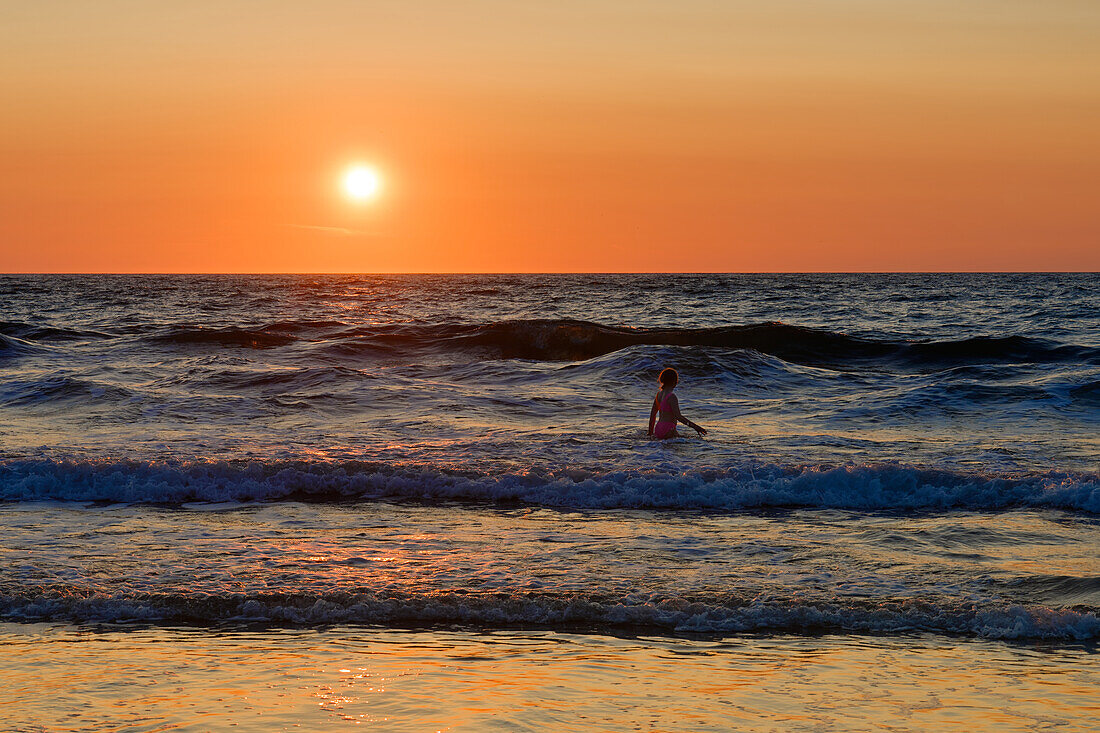 Großbritannien, West Wales, Bezirk Ceredigion, Llangrannog, Baden bei Sonnenuntergang im Meer