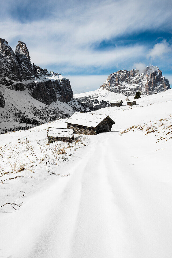 Schneebedeckte Almhütten vor Cirspitzen und Blick zum Langkofel im Winter, Grödner Joch, Grödnertal, Dolomiten, Südtirol, Italien