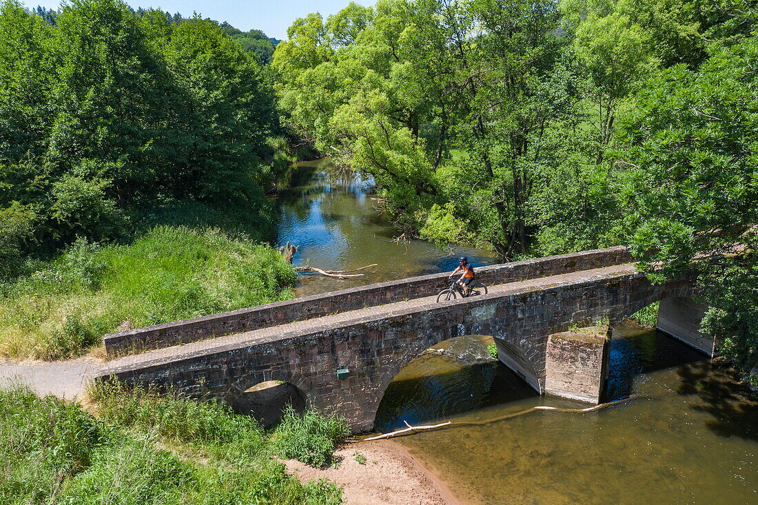 Aerial view of a cyclist crossing a stone bridge over the Haune River in the Hessisches Kegelspiel region, Burghaun Rothenkirchen, Rhön, Hesse, Germany