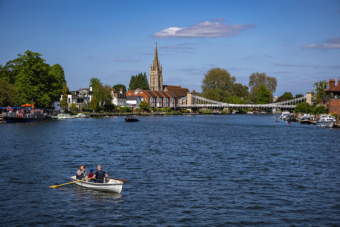 Rowing boat on the River Thames with All Saints Church and Marlow Suspension Bridge behind, Marlow, Buckinghamshire, England, United Kingdom