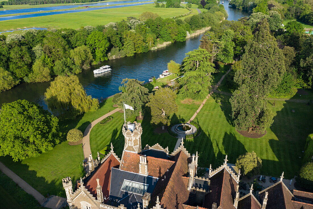 Aerial view of a Le Boat Horizon 4 houseboat passing the Oakley Court Hotel along the River Thames, Water Oakley, near Windsor, Berkshire, England, United Kingdom