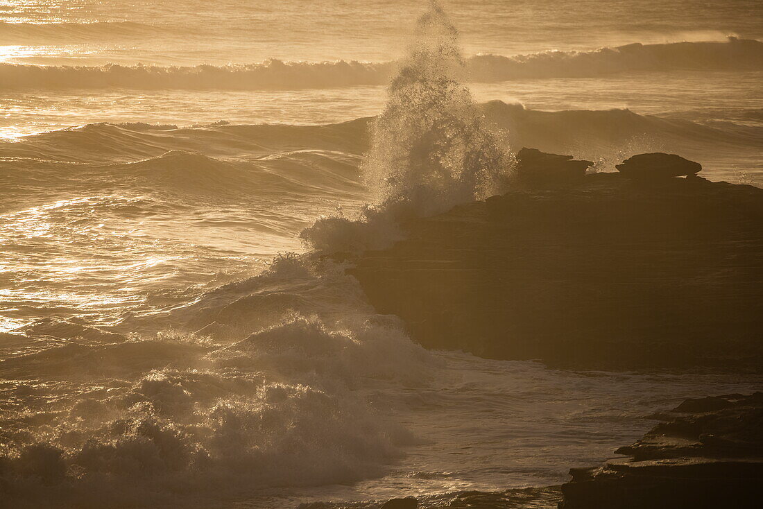 Wellen brechen auf die felsige Küste und den Strand im Walker Bay Nature Reserve bei Sonnenuntergang, Gansbaai De Kelders, Westkap, Südafrika
