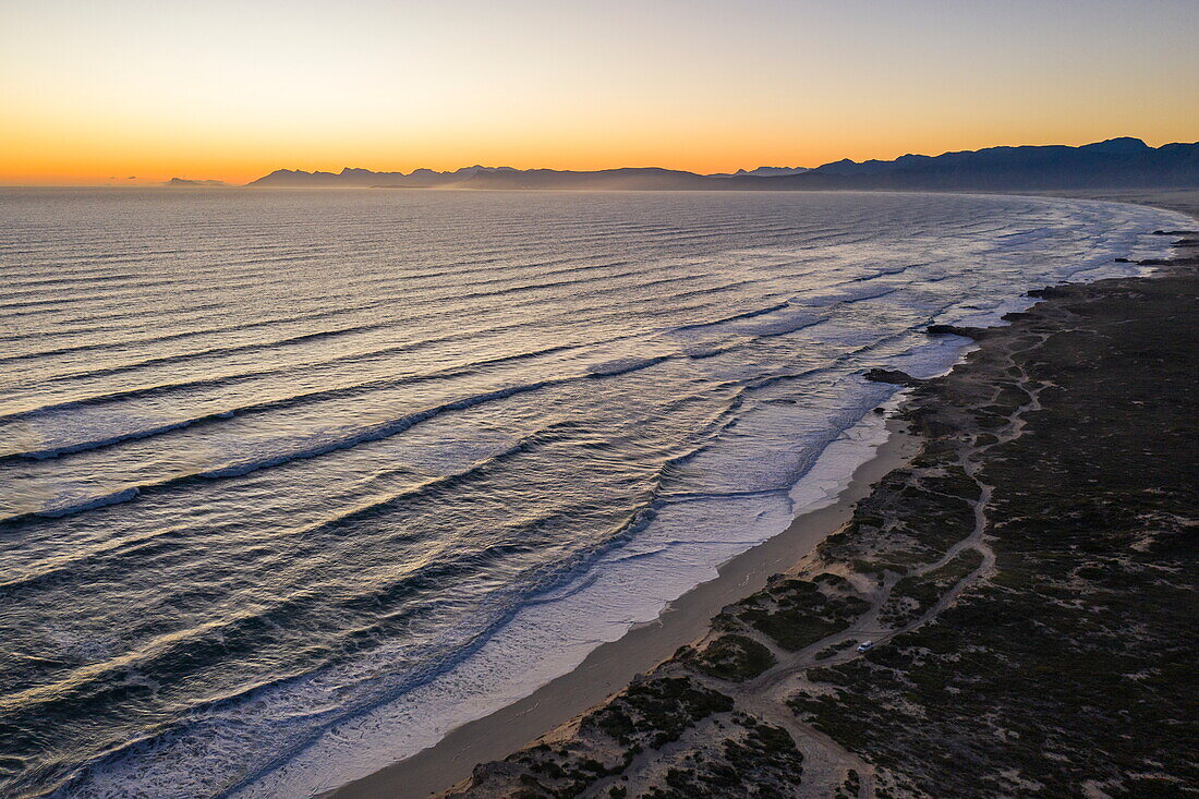 Aerial view of waves breaking onto the coast and beach at Walker Bay Nature Reserve at sunset, Gansbaai De Kelders, Western Cape, South Africa