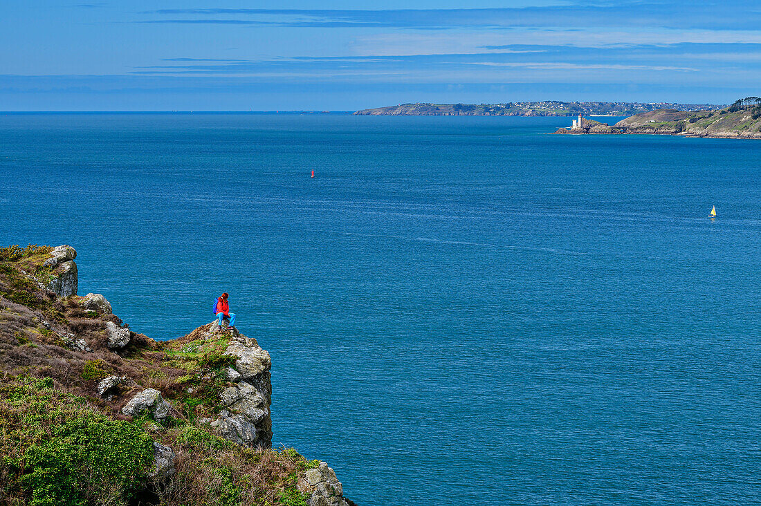 Frau beim Wandern sitzt auf Felsvorsprung und blickt auf Meerenge von Brest, GR 34, Zöllnerweg, Sentier Côtier, Halbinsel Crozon, Atlantikküste, Bretagne, Frankreich