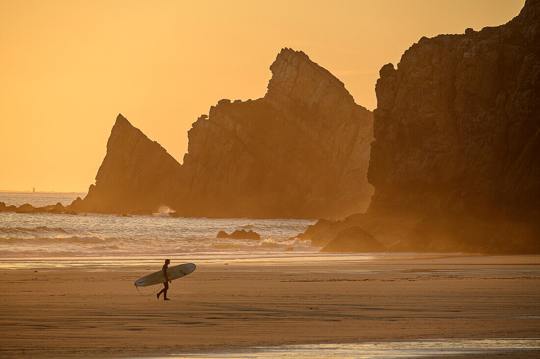 Surfer geht über den Strand Plage de Pen Hat, Pointe du Toulinguet im Hintergrund, Camaret-sur-Mer, GR 34, Zöllnerweg, Sentier Côtier, Halbinsel Crozon, Atlantikküste, Bretagne, Frankreich