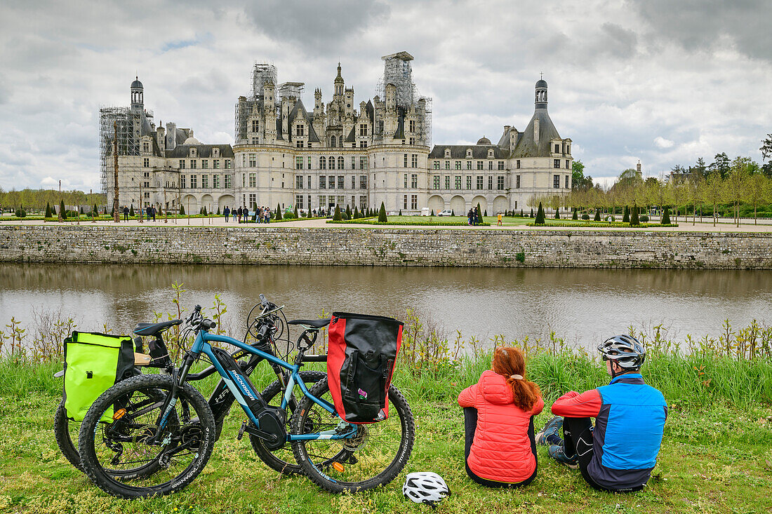 Man and woman cycling on the Loire cycle path take a break and look at the Château de Chambord, Loire Castles, Loire Valley, UNESCO World Heritage Site Loire Valley, France