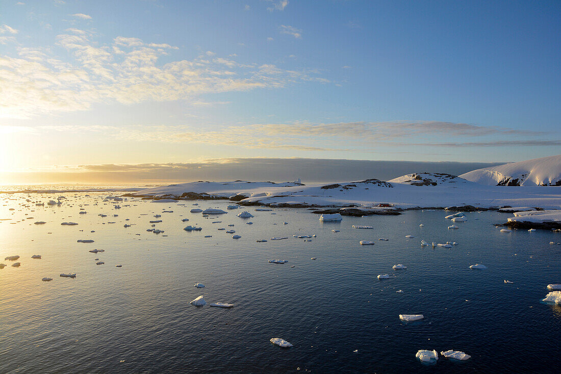 Antarktis; antarktische Halbinsel; bei Petermann Island; auf der Fahrt Richtung Port Charcot; Schnee bedeckte Hügel; kleinere Eisschollen treiben vor der Küste; Abendstimmung; Sonne geht nicht mehr unter