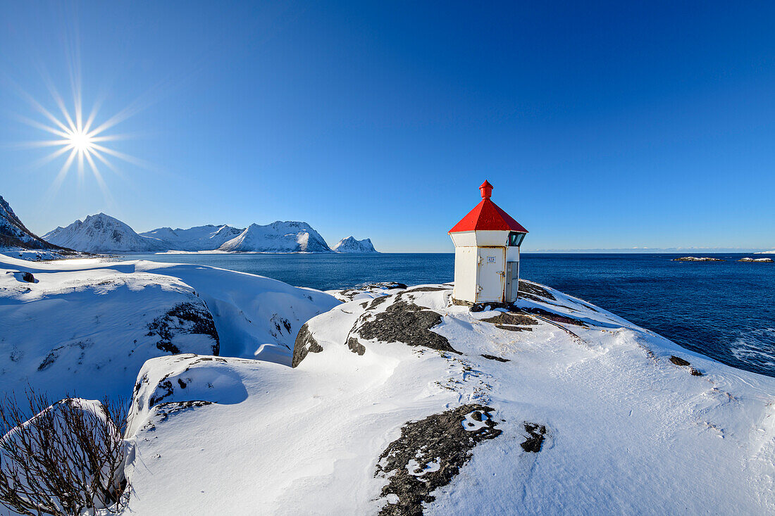 Lighthouse stands on headland with snowy mountains in the background, Senja, Troms og Finnmark, Norway