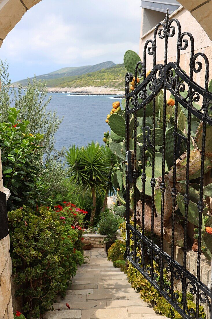 Blick durch Gartentor auf einen mediteranen Garten, im Hintergrund Meer, Dalmatien, Kroatien