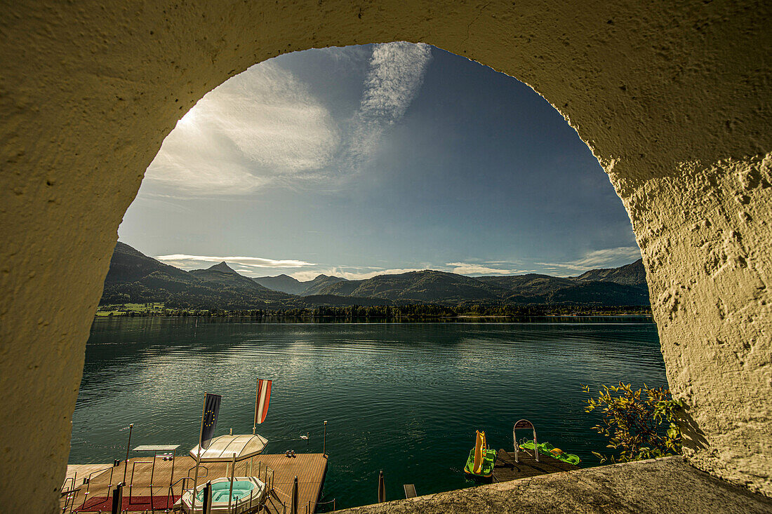 Blick durch einen Bogen auf eine Badeanlage am Wolfgangsee und auf die Berge des Salzkammerguts, St. Wolfgang, Österreich