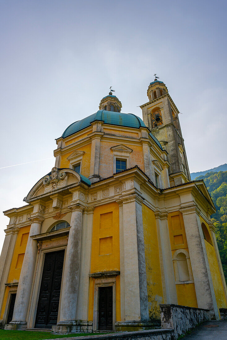 Kirche des Heiligen Kreuzes vor blauem, klarem Himmel an einem sonnigen Tag in Riva San Vitale, Tessin, Schweiz
