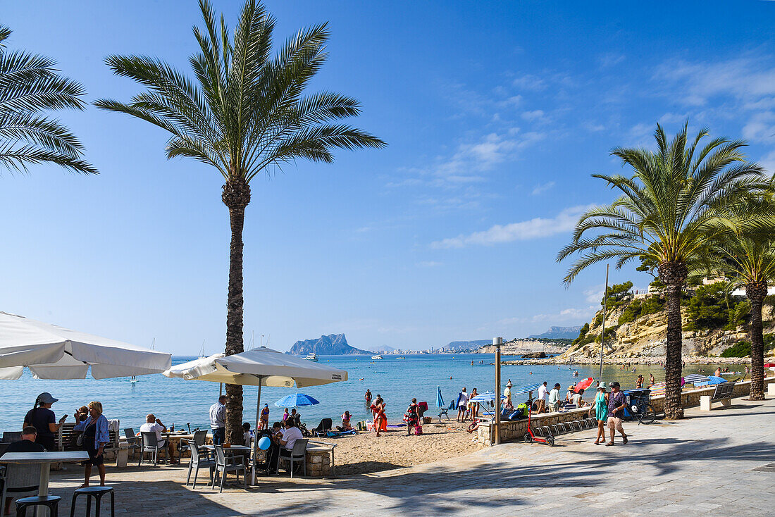 Menschen im Cafe und am Strand El Portet, im Hintergrund Blilck auf Calpe mit dem Fels Penon de Ifach, Moraira, Costa Blanca, Provinz Alicante, Spanien