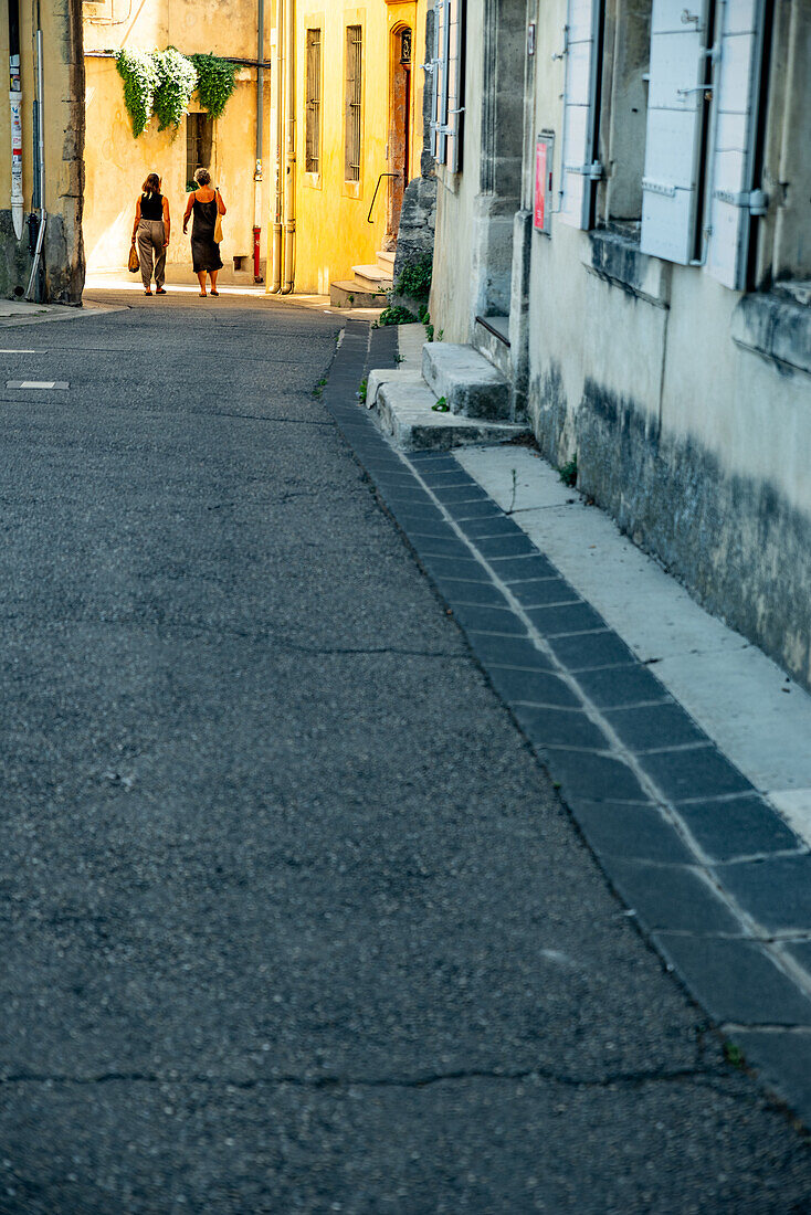 Two women walking through a arched stone gate in the medieval city of Arles, France