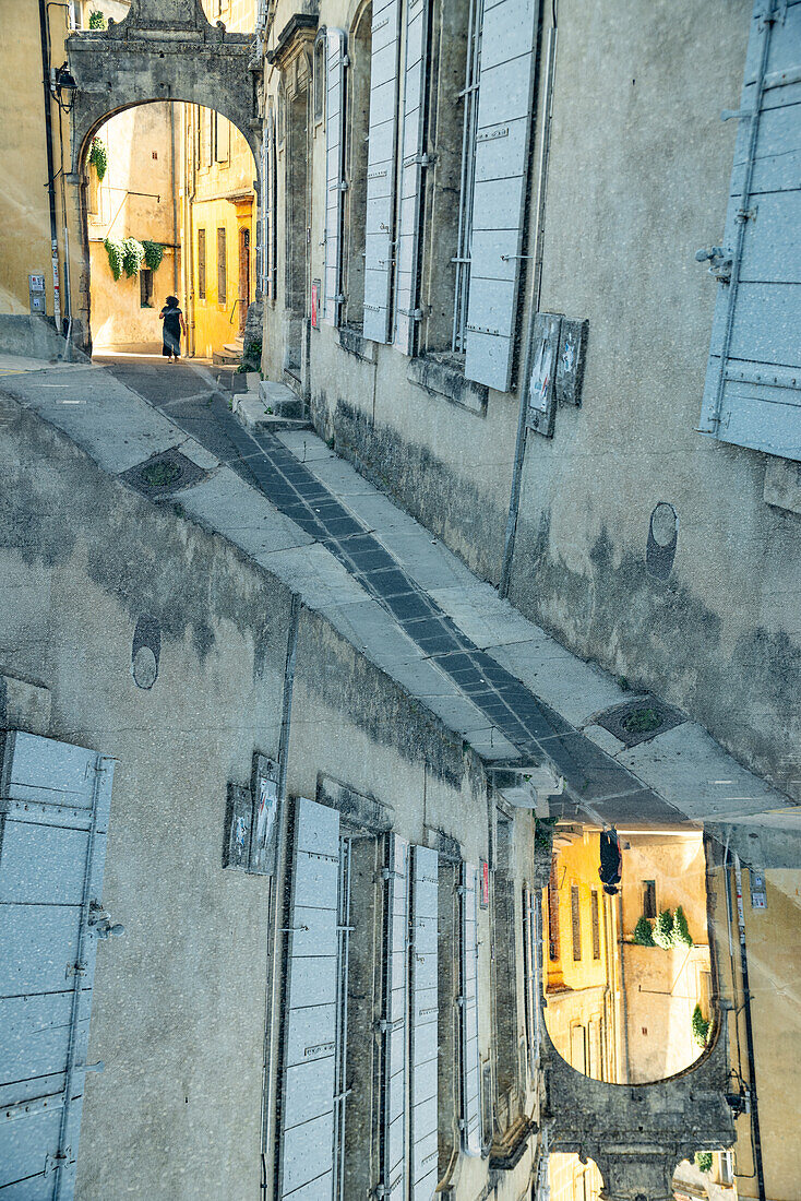 Graphic double exposure of a person walking through a arched gate in the medieval town of Arles, France.