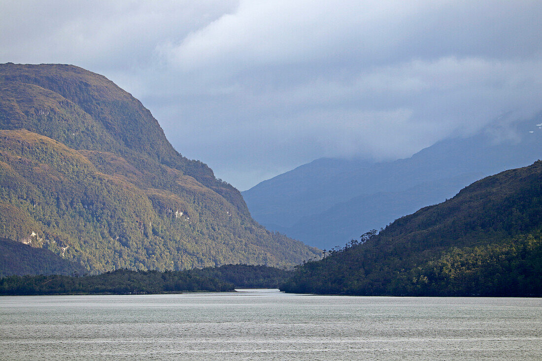 Chile; Südchile; Region Magallanes; Gebirge der südlichen Cordillera Patagonica; auf der Navimag Fähre durch die patagonischen Fjorde; Angostura Inglesa; Sonne und Wolken wechseln sich ab; Blick auf die bewaldeten Berghänge