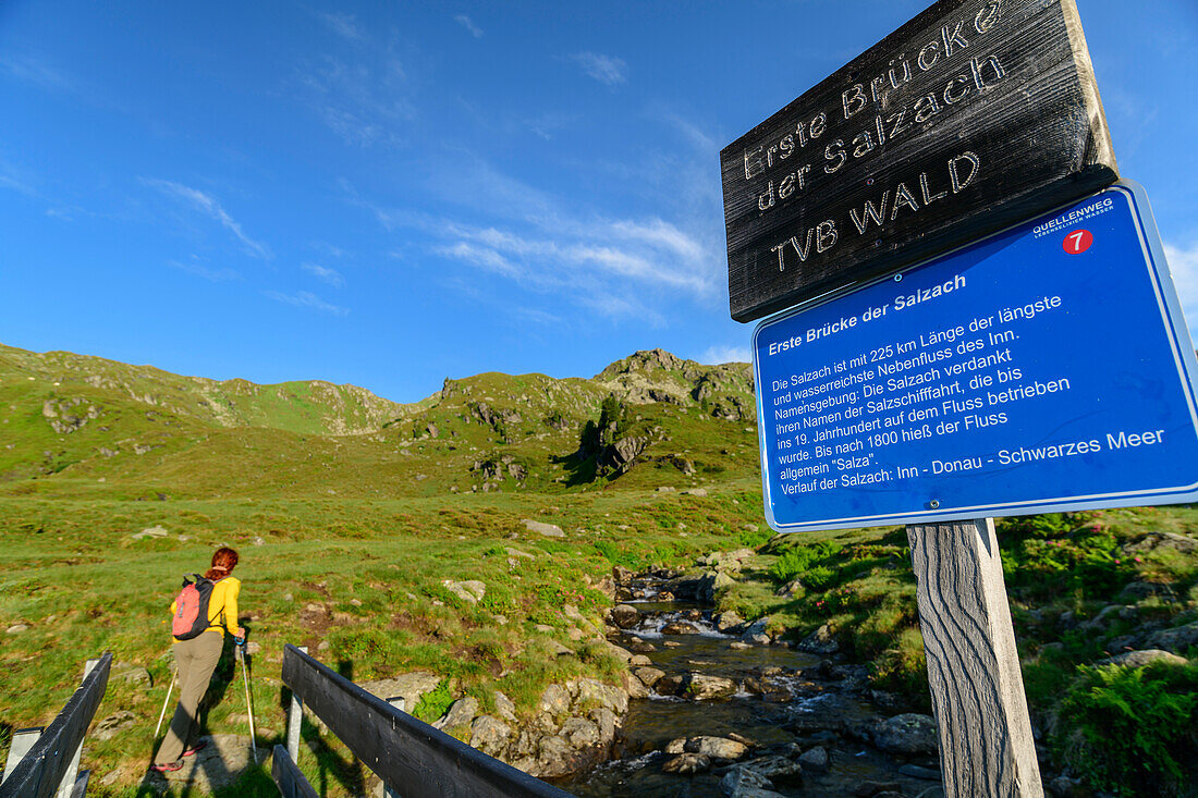 Woman hiking climbs up to the Salzachgeier, bridge over the Salzach and signs in the foreground, Salzachquelle, Kitzbühel Alps, Tyrol, Austria