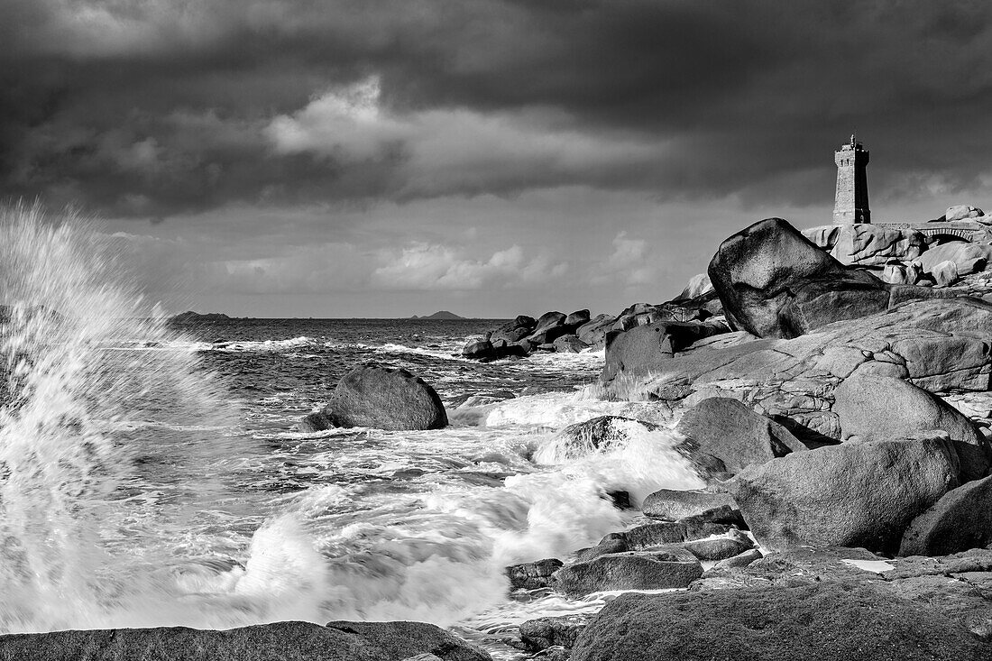 Sea surf hits granite rocks with Phare de Men Ruz lighthouse in the background, Cote de Granit Rose, Pink Granite Coast, Ploumanac&#39;h, Ploumanach, Brittany, France