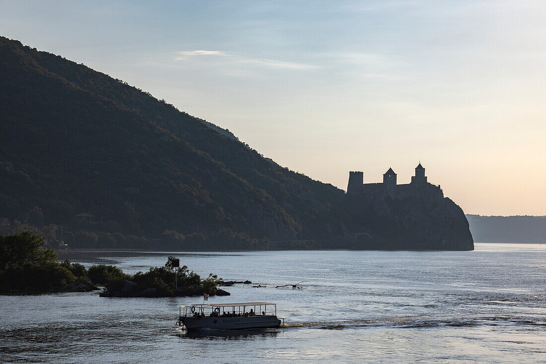 Silhouette von Ausflugsboot in der Schlucht Eisernes Tor der Donau mit der Festung Golubac in der Ferne, Golubac, Braničevo, Serbien, Europa