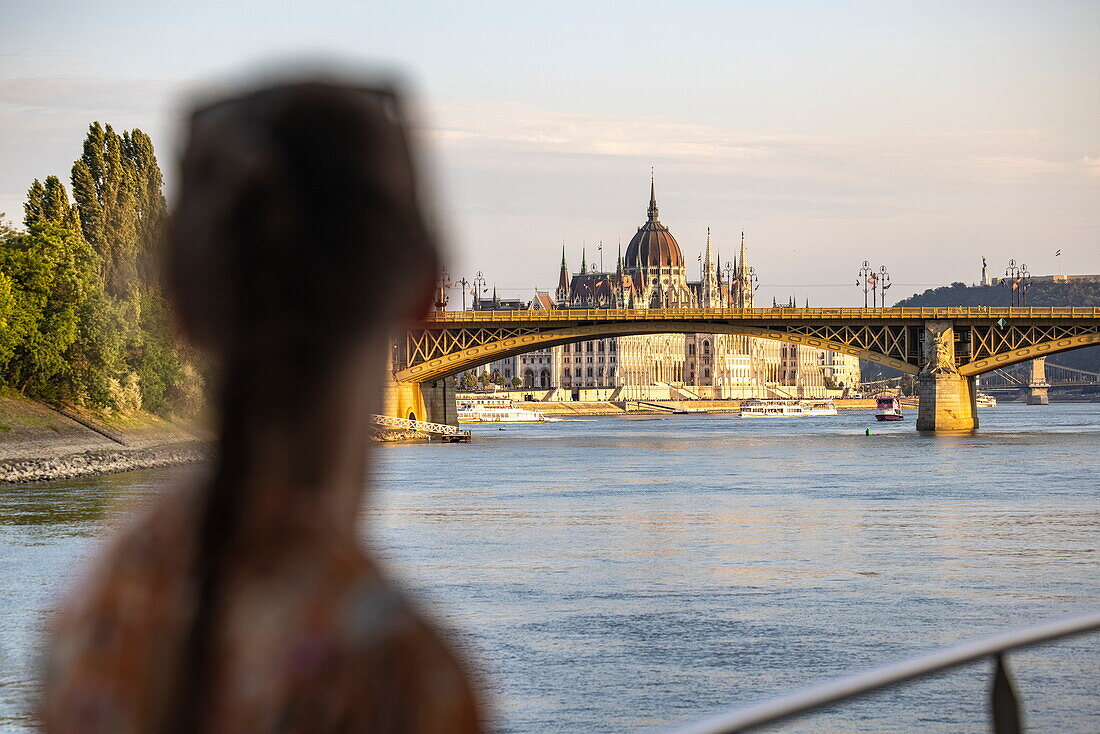 Hungarian Parliament building on the Danube in the late afternoon sun, seen from river cruise ship Viktoria (nicko cruises) with the silhouette of a teenage girl in the foreground, Budapest, Pest, Hungary, Europe