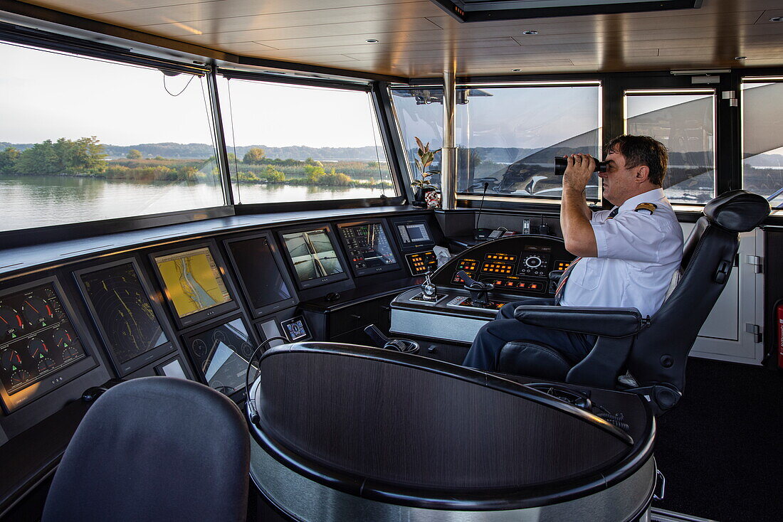 Kapitän blickt durch ein Fernglas auf Brücke von Flusskreuzfahrtschiff nickoVISION (nicko cruises) auf der Donau, in der Nähe von Bratislava, Bratislava, Slowakei, Europa