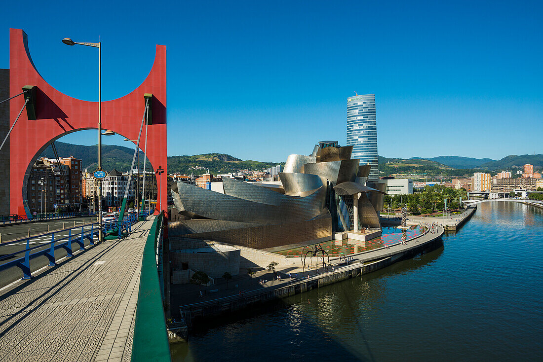 Brücke Puente La Salve mit rotem Torbogen über den Fluss Ría de Bilbao neben Guggenheim Museum und Stadtansicht, Bilbao, Provinz Bizkaia, Baskenland, Spanien