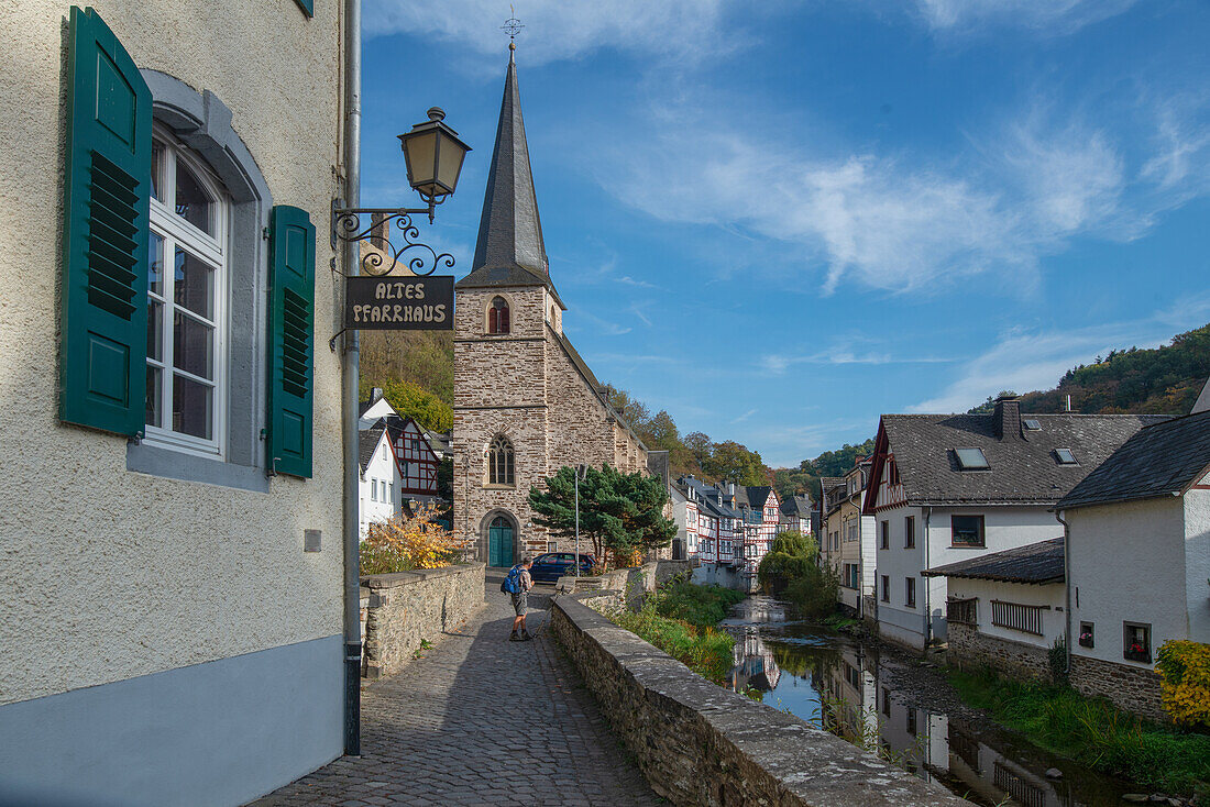 Fachwerkhäuser und die Heilige Dreifaltigkeitskirche säumen das vom Etzbach durchzogene Monreal, Rheinland-Pfalz, Deutschland