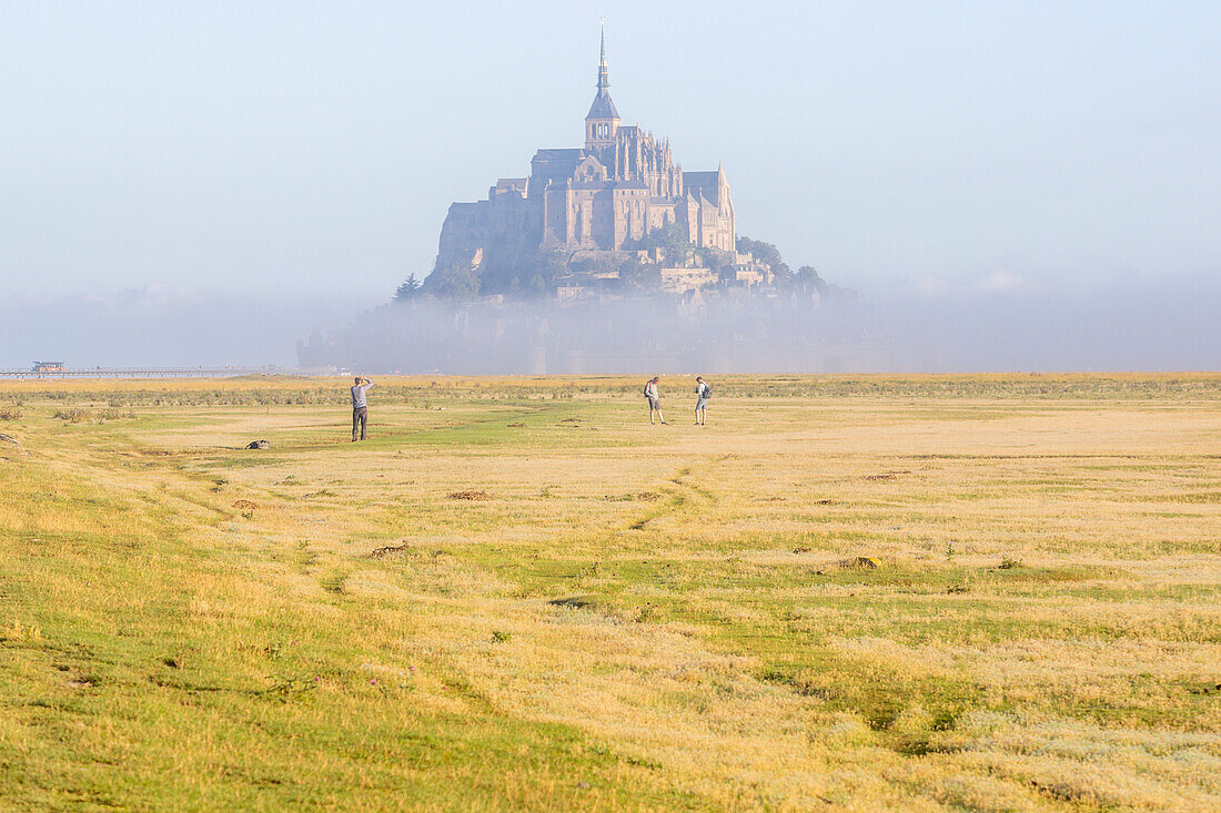 Spaziergänger auf Wiese und Nebelschwaden vor Mont Saint-Michel, Département Manche, Normandie, Frankreich