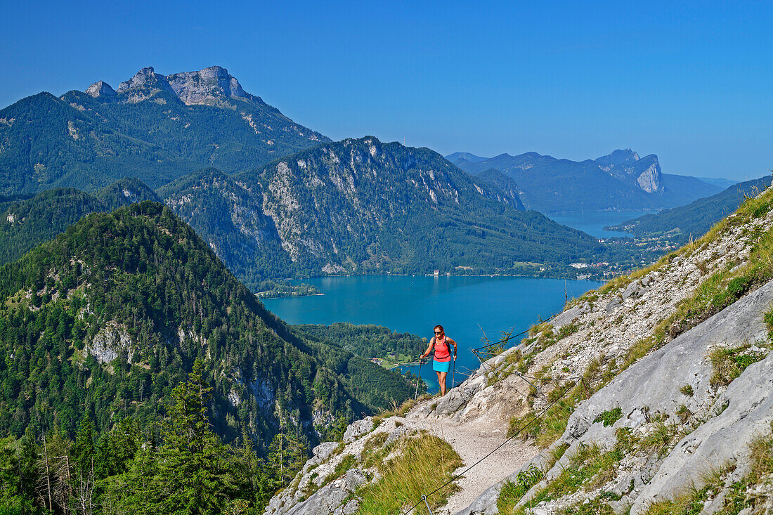 Woman hiking climbs up to Schoberstein, Attersee and Mondsee in the background, from Schoberstein, Salzkammergut Mountains, Salzkammergut, Upper Austria, Austria