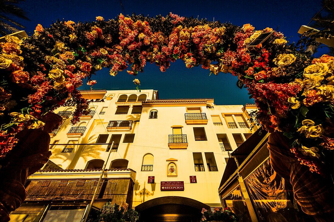  View through an arch of roses to the Hotel Park Plaza Suites Apartments in the evening light, Puerto Banús, Marbella, Costa del Sol, Andalusia, Spain 