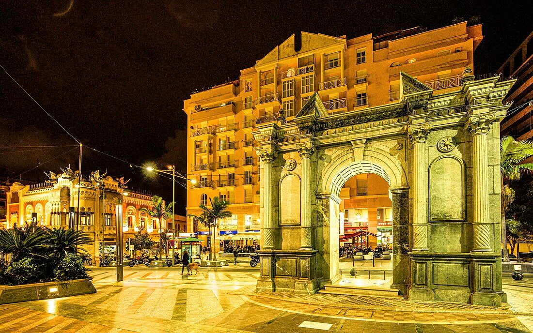 Triumphbogen an der Plaza de los Reyes mit Blick auf ein Café und die Casa de los Dragones am Abend, Ceuta, Straße von Gibraltar, Spanien