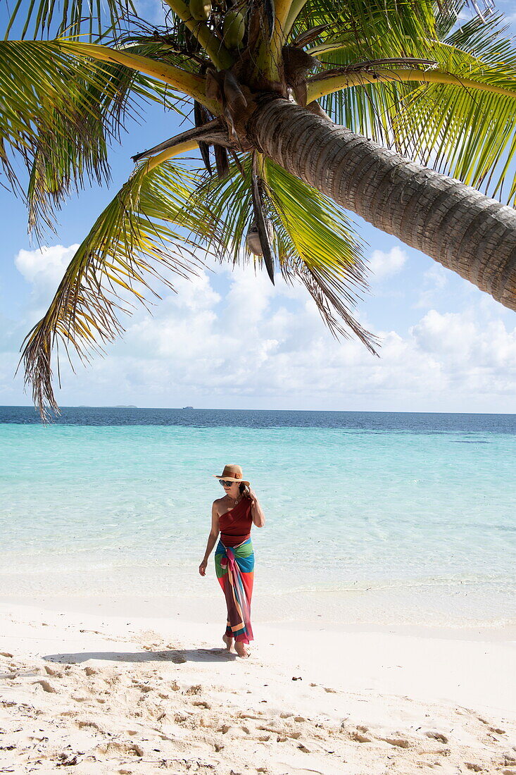 Kokospalme und Frau in buntem Kleid am Strand, Bijoutier Island, Alphonse Group, Äußere Seychellen, Seychellen, Indischer Ozean