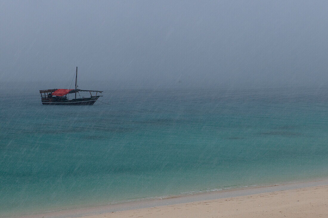 Traditionelles Dhau-Segelboot vor Anker am Strand bei Regenschauer, in der Nähe von Stonetown, Sansibar-Stadt, Sansibar, Tansania, Afrika