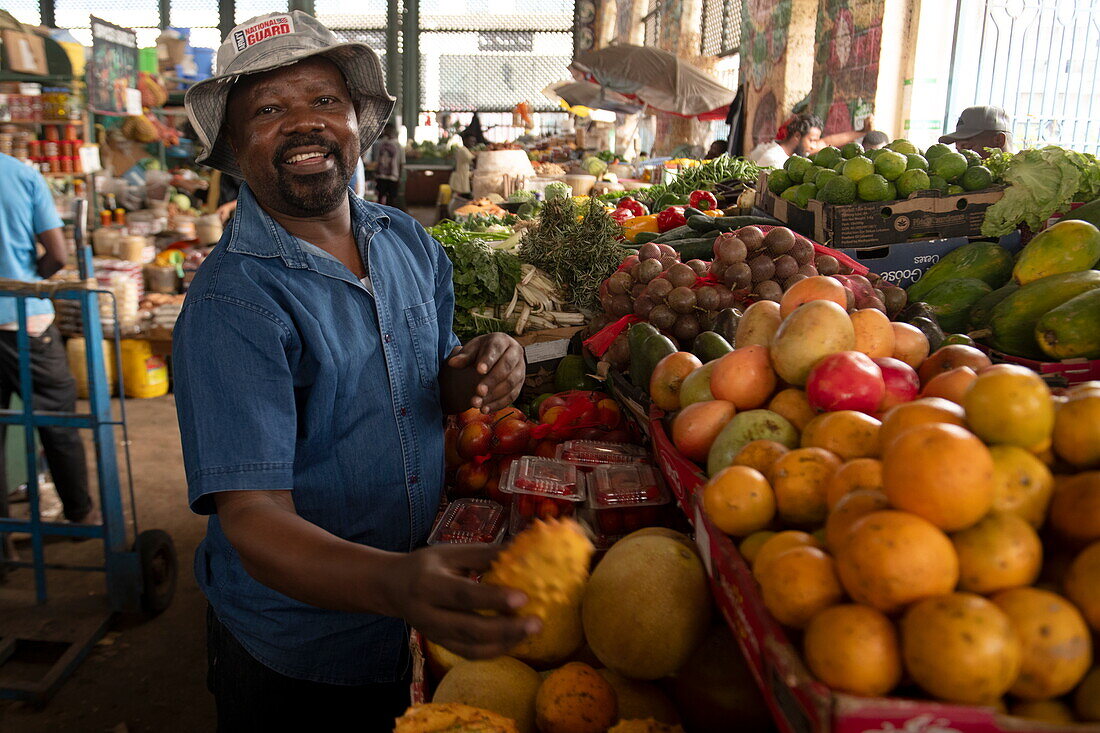 Fröhlicher Mann an einem Obst- und Gemüsestand in der Markthalle, Mombasa, Kenia, Afrika