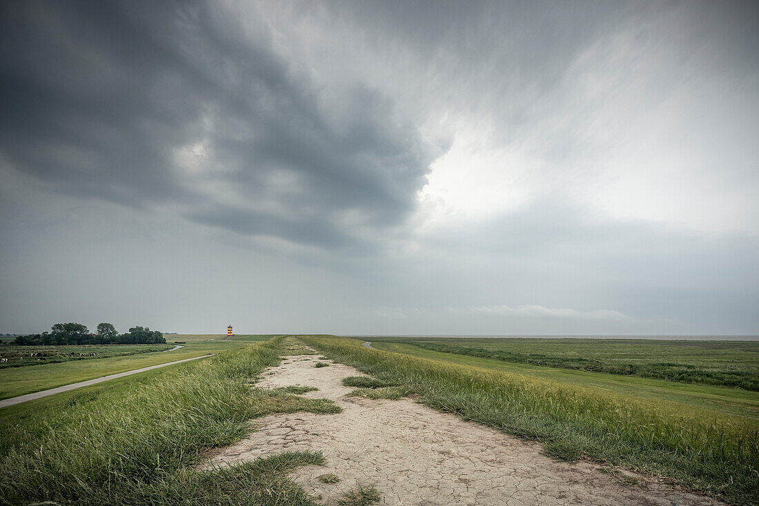  Dike and salt marshes at the Pilsum lighthouse under storm clouds, Krummhörn, East Frisia, Lower Saxony, Germany, Europe 