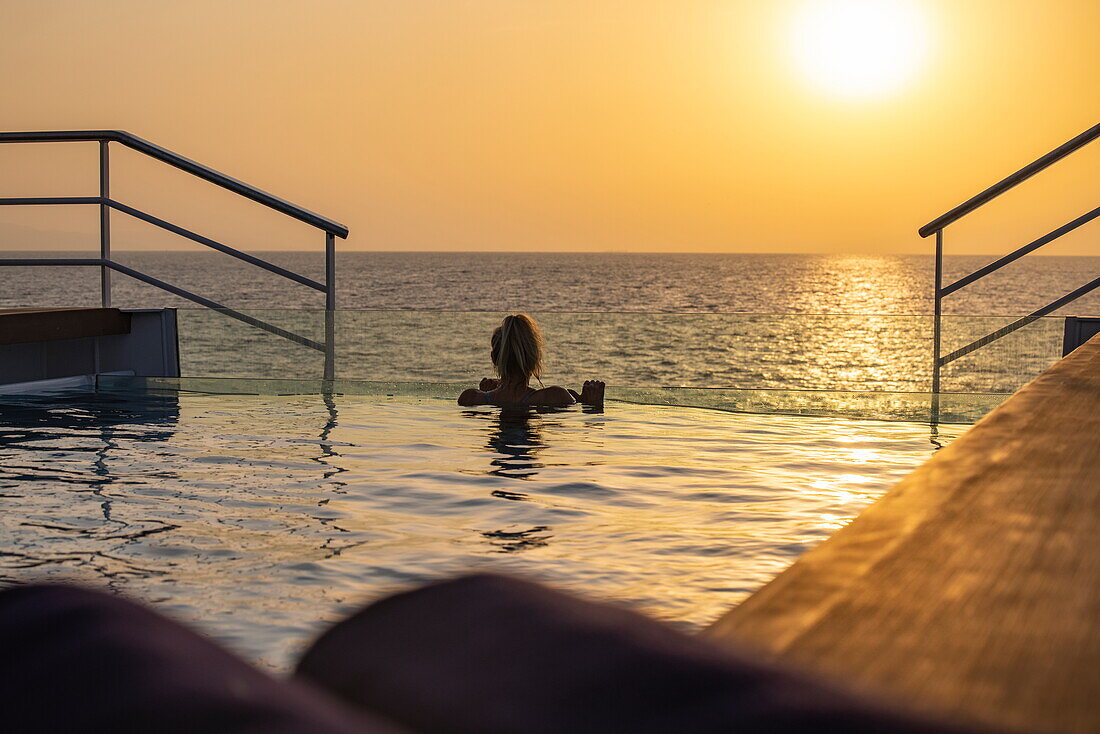 Frau entspannt sich im Schwimmbad auf dem Achterdeck des Expeditionskreuzfahrtschiffes SH Diana (Swan Hellenic) bei Sonnenuntergang, in der Nähe des Jemen, Golf von Aden, Ostafrika