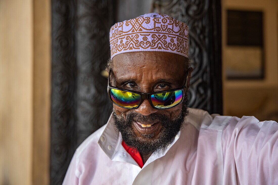 Lächelnder Mann mit muslimischem Taqiyah-Hut und bunt reflektierender Sonnenbrille, Lamu, Insel Lamu, Kenia, Afrika