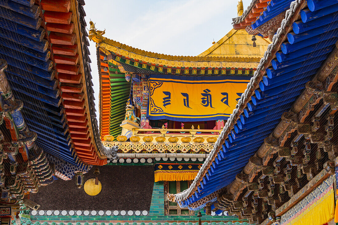 Bunte Dächer mit Balken und Ornamenten sowie spektakulären Verzierungen an einem Tempel im Kloster Kumbum Jampaling, Xining, China