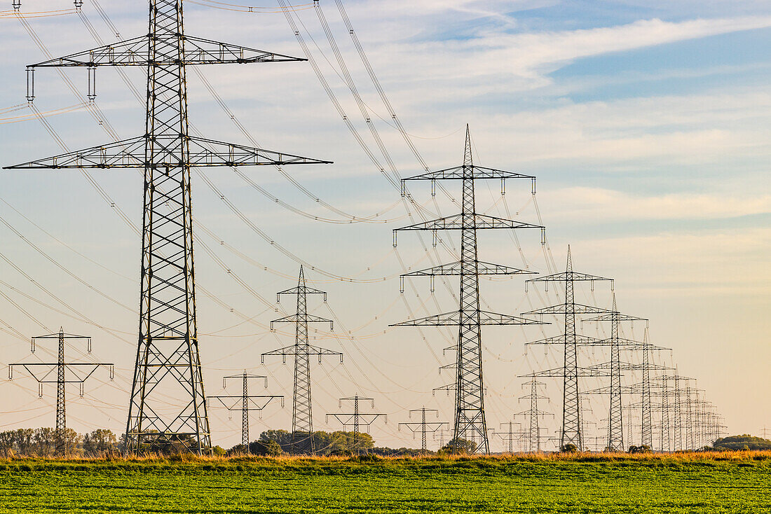  Countless electricity pylons and overhead power lines in rural areas in the evening at sunset, Germany 