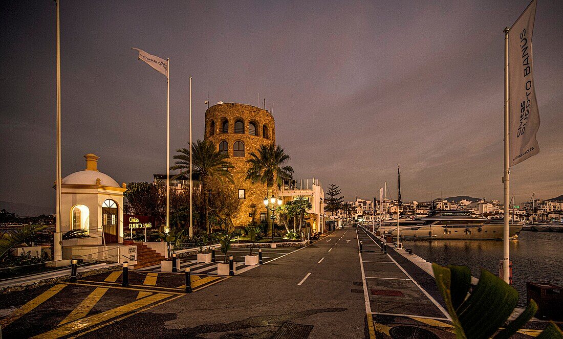 Promenade am Yachthafen von Puerto Banús bei Nacht mit historischem Turm und der Kapelle zu Ehren der Senora del Carmen, Puerto Banús, Marbella, Costa del Sol, Spanien