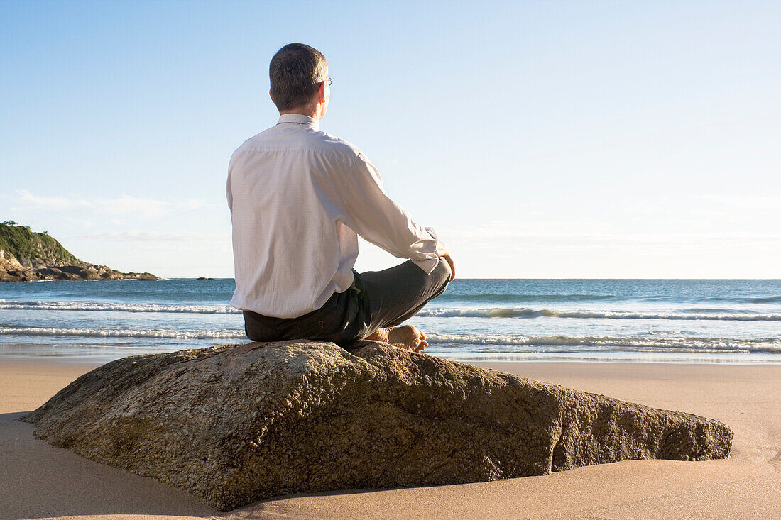 Geschäftsmann meditiert auf einem Felsen am Strand, Bombinhas, Santa Catarina, Brasilien