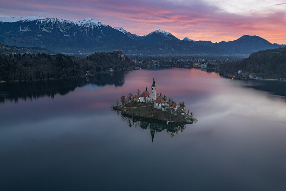 Luftaufnahme der Marienkirche im Bleder See und der verschneiten Berge kurz vor Sonnenuntergang in Bled, Slowenien, Europa.